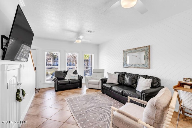 living room featuring ceiling fan, a textured ceiling, light tile patterned flooring, visible vents, and baseboards