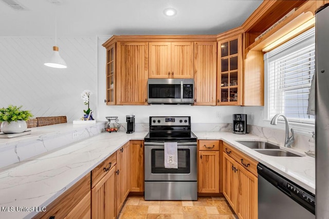 kitchen featuring light stone counters, stainless steel appliances, hanging light fixtures, stone finish flooring, and a sink