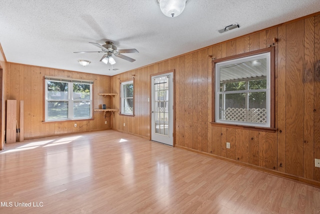 unfurnished room featuring ceiling fan, wood walls, a textured ceiling, and light wood-type flooring