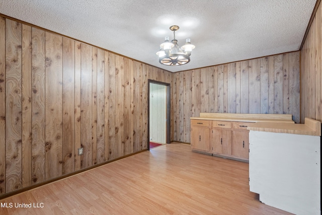 interior space featuring a chandelier, wooden walls, a textured ceiling, and light hardwood / wood-style floors