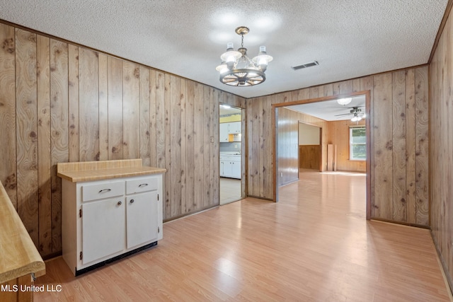 interior space featuring wooden walls, a textured ceiling, light wood-type flooring, and ceiling fan with notable chandelier