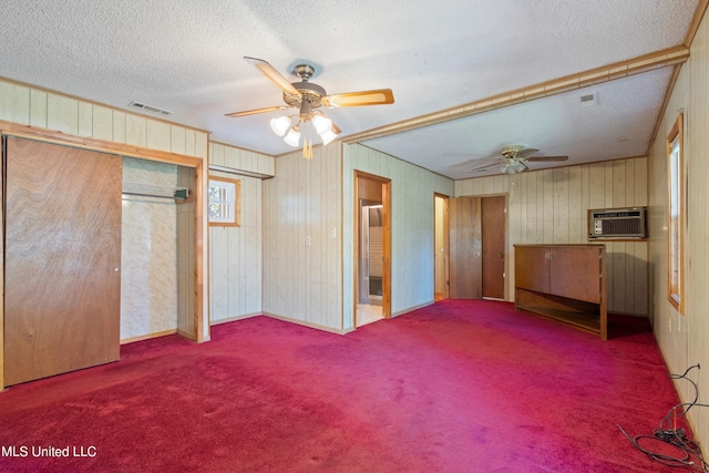 unfurnished bedroom with a wall unit AC, wooden walls, carpet, a textured ceiling, and ceiling fan