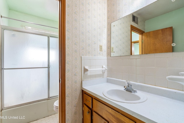 full bathroom featuring toilet, bath / shower combo with glass door, vanity, and tasteful backsplash