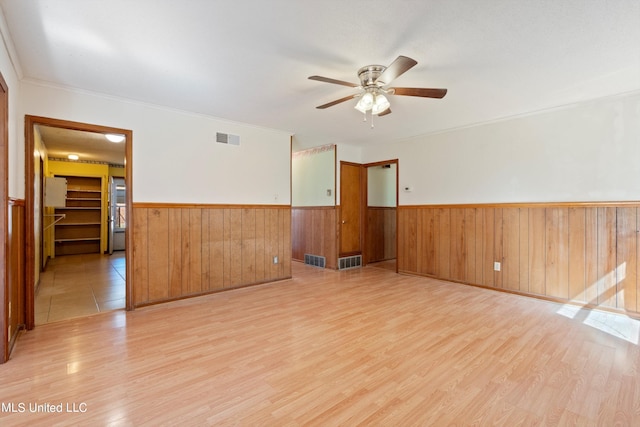 spare room featuring ornamental molding, wooden walls, light hardwood / wood-style flooring, and ceiling fan