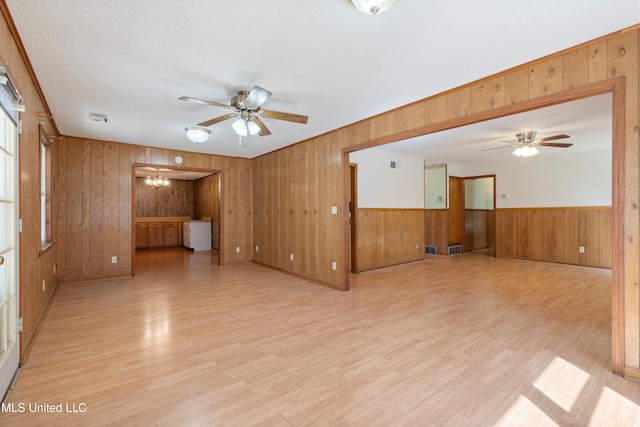 empty room with wooden walls, ceiling fan with notable chandelier, and light hardwood / wood-style floors