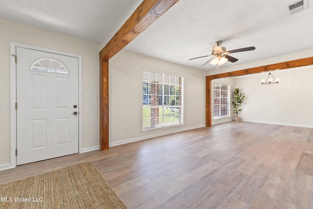 entrance foyer with light hardwood / wood-style floors, beamed ceiling, a textured ceiling, and ceiling fan with notable chandelier