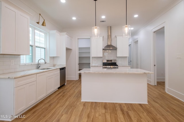 103 E 2nd St, Pass Christian, MS 39571 - kitchen with light wood-style floors, appliances with stainless steel finishes, wall chimney exhaust hood, and white cabinetry