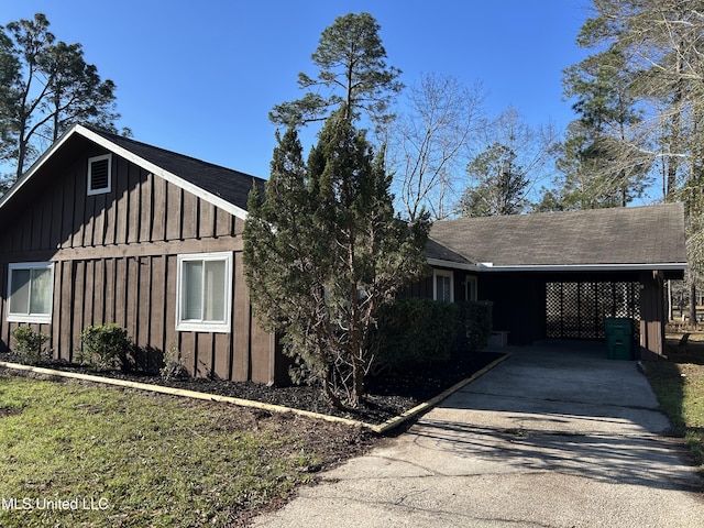 view of side of property with board and batten siding, driveway, a carport, and a shingled roof