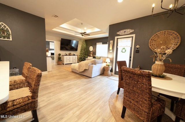 living area featuring a raised ceiling, baseboards, visible vents, and light wood finished floors