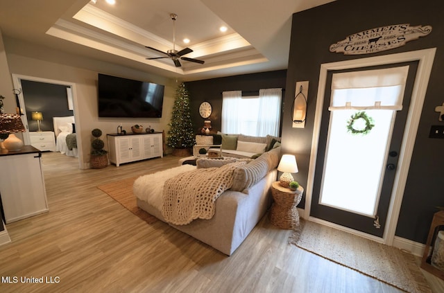 living area with ornamental molding, light wood-style flooring, a ceiling fan, and a tray ceiling