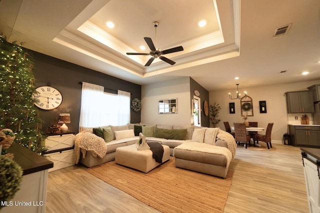 living room with ceiling fan with notable chandelier, visible vents, a raised ceiling, and light wood-type flooring