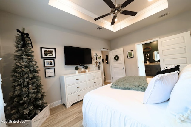 bedroom with visible vents, ornamental molding, baseboards, a tray ceiling, and light wood-style flooring