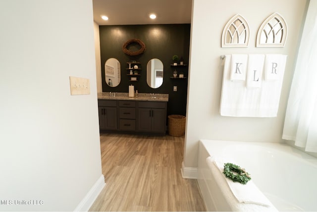 bathroom with double vanity, a garden tub, wood finished floors, a sink, and baseboards