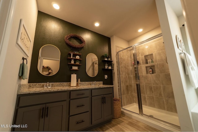 bathroom with double vanity, a stall shower, wood finished floors, a sink, and recessed lighting