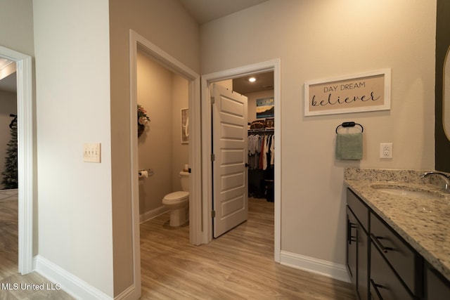 full bath with a walk in closet, vanity, toilet, baseboards, and wood finished floors