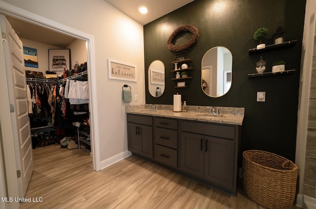 full bath featuring baseboards, a sink, wood finished floors, and double vanity