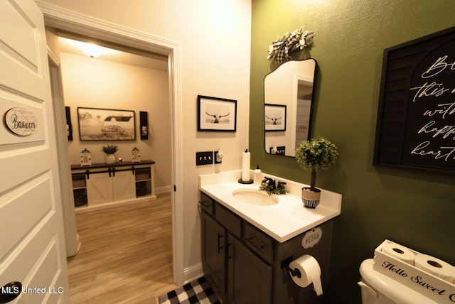 half bathroom with toilet, baseboards, wood finished floors, and vanity