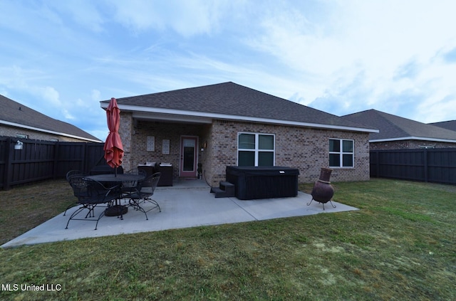 back of house featuring a hot tub, a patio, a fenced backyard, and a lawn