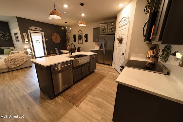kitchen featuring open floor plan, light wood-type flooring, light countertops, a sink, and appliances with stainless steel finishes