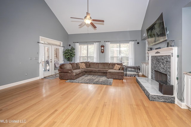 living room featuring a tile fireplace, high vaulted ceiling, ceiling fan, light wood-type flooring, and french doors