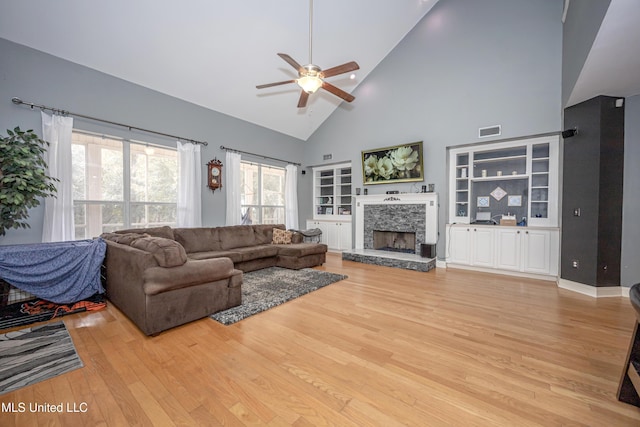 living room featuring built in features, ceiling fan, high vaulted ceiling, a fireplace, and light wood-type flooring