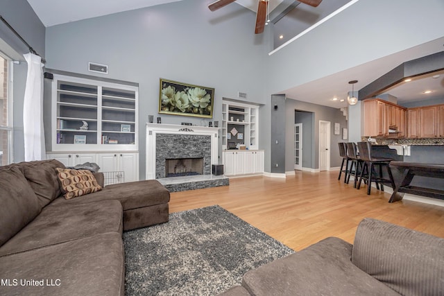 living room featuring ceiling fan, a fireplace, light wood-type flooring, and built in shelves