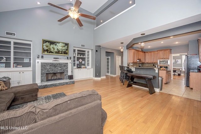 living room with a stone fireplace, light hardwood / wood-style flooring, and ceiling fan