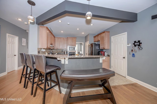 kitchen with beamed ceiling, appliances with stainless steel finishes, kitchen peninsula, and light stone countertops