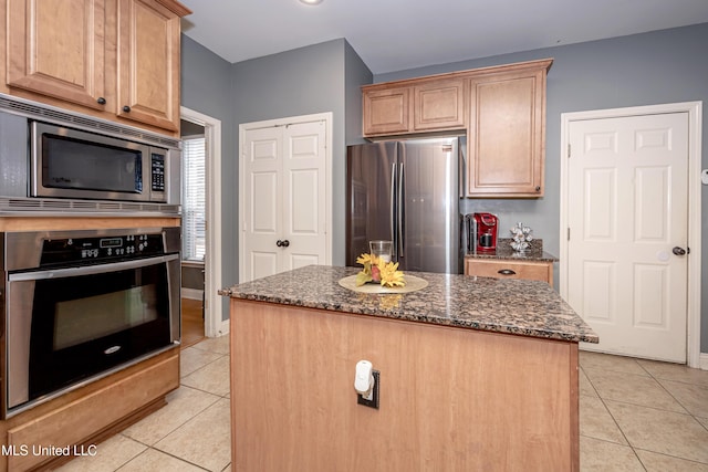 kitchen featuring light tile patterned flooring, stainless steel appliances, a kitchen island, and dark stone counters