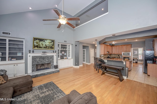 living room with a fireplace, vaulted ceiling, ceiling fan, and light wood-type flooring