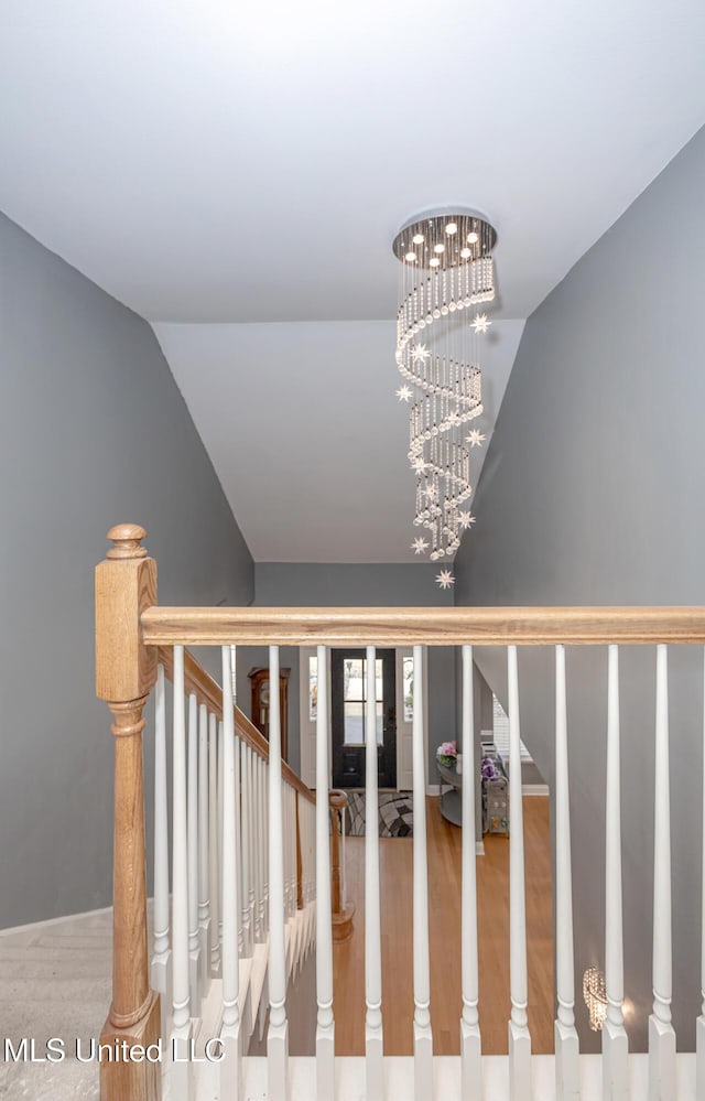 stairway featuring vaulted ceiling, hardwood / wood-style floors, and a notable chandelier