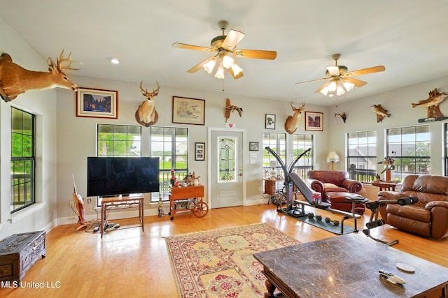 living room featuring baseboards, light wood-type flooring, and a ceiling fan