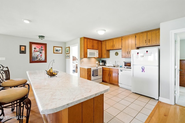 kitchen featuring light countertops, white appliances, a sink, light tile patterned flooring, and brown cabinetry