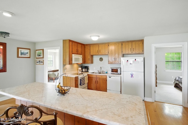 kitchen featuring light countertops, light wood finished floors, baseboards, white appliances, and a sink