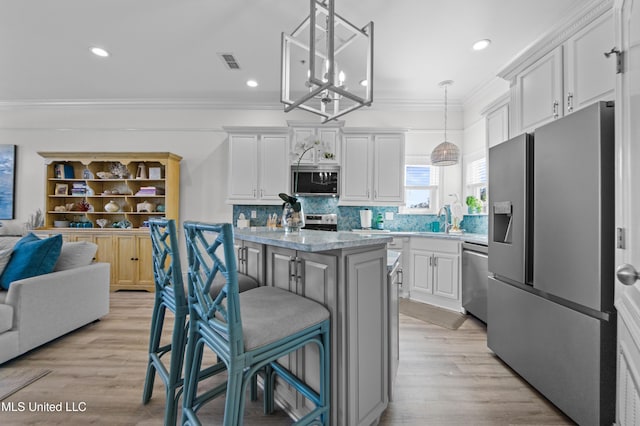 kitchen featuring a center island, stainless steel appliances, visible vents, ornamental molding, and a kitchen bar