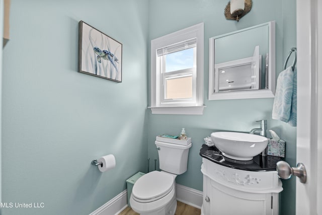 half bathroom featuring toilet, baseboards, wood finished floors, and vanity