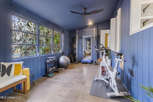 exercise room with tile patterned flooring, ceiling fan, wood walls, and lofted ceiling