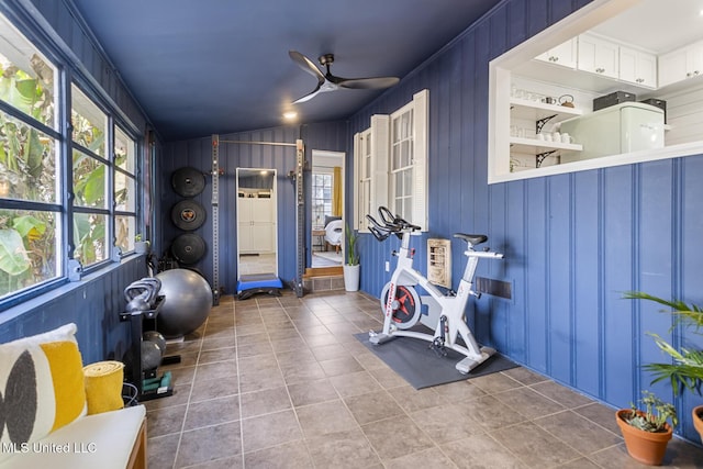 workout area with tile patterned floors, ceiling fan, and wood walls