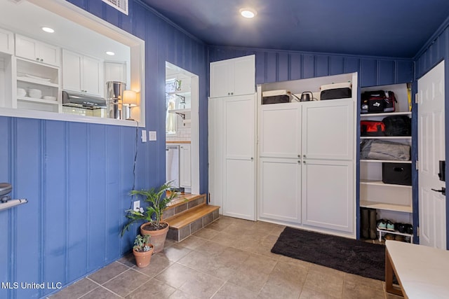 mudroom featuring lofted ceiling, light tile patterned flooring, ornamental molding, and wooden walls