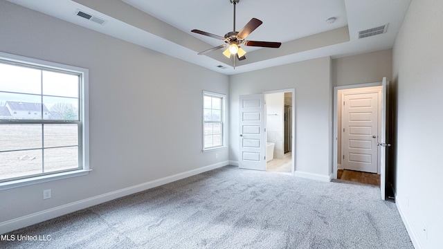 unfurnished bedroom with ceiling fan, ensuite bathroom, light colored carpet, and a raised ceiling