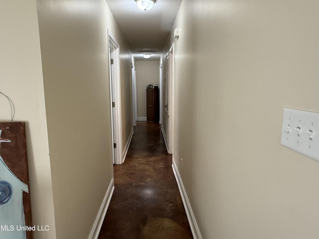 hall featuring concrete flooring and baseboards