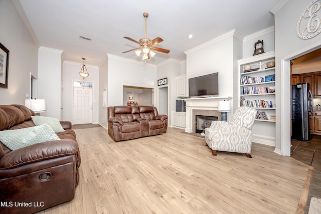 living room with a tiled fireplace, crown molding, visible vents, and light wood finished floors