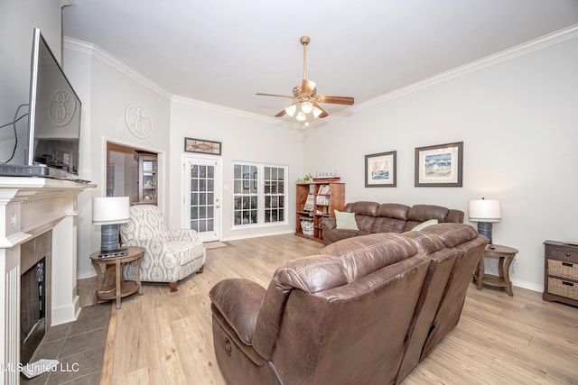 living room featuring a tiled fireplace, a ceiling fan, wood finished floors, and ornamental molding