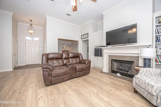 living room with a ceiling fan, visible vents, ornamental molding, light wood-style floors, and a tiled fireplace