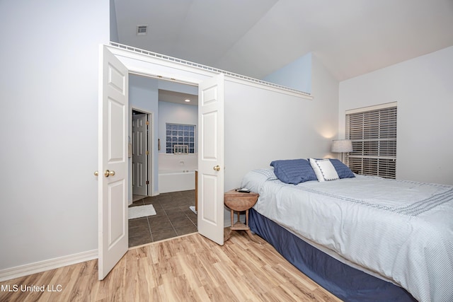 bedroom featuring vaulted ceiling, light wood-style floors, visible vents, and baseboards