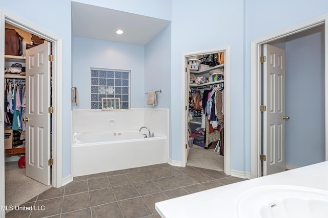 bathroom with tile patterned floors, a walk in closet, a garden tub, baseboards, and vanity