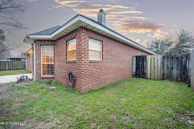 view of property exterior with brick siding, a fenced backyard, a chimney, and a yard