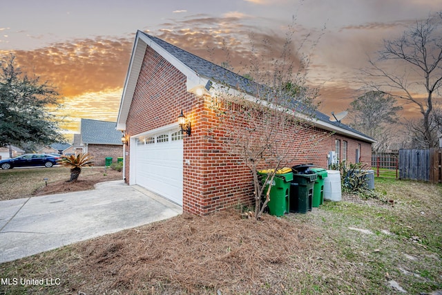 property exterior at dusk with a garage, brick siding, driveway, and fence