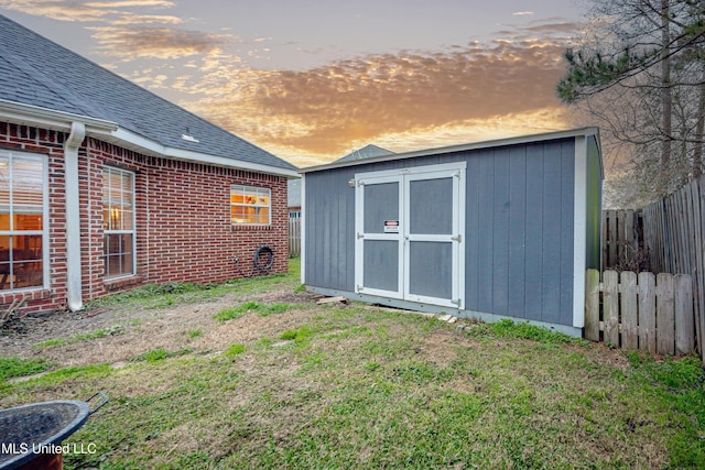 outdoor structure at dusk with an outbuilding, a storage unit, fence, and a lawn