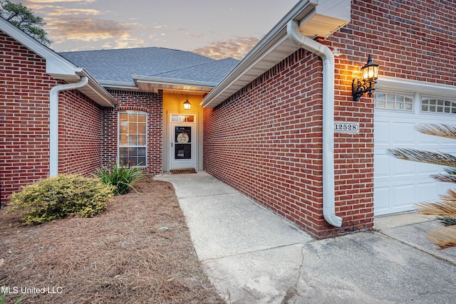 view of exterior entry featuring brick siding, a garage, and roof with shingles